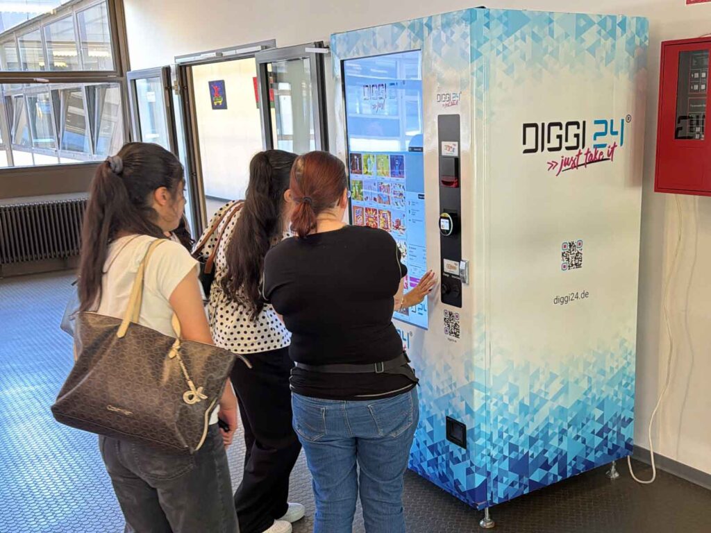 Schülerinnen bedienen den Touchscreen eines DIGGI 24 Snackautomaten in der Schule